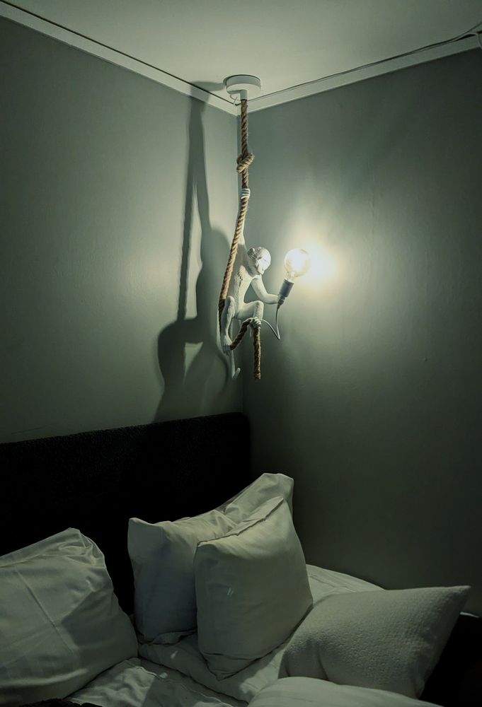 A hotel room with a light fixture shaped like a monkey on a rope, just over the bed...