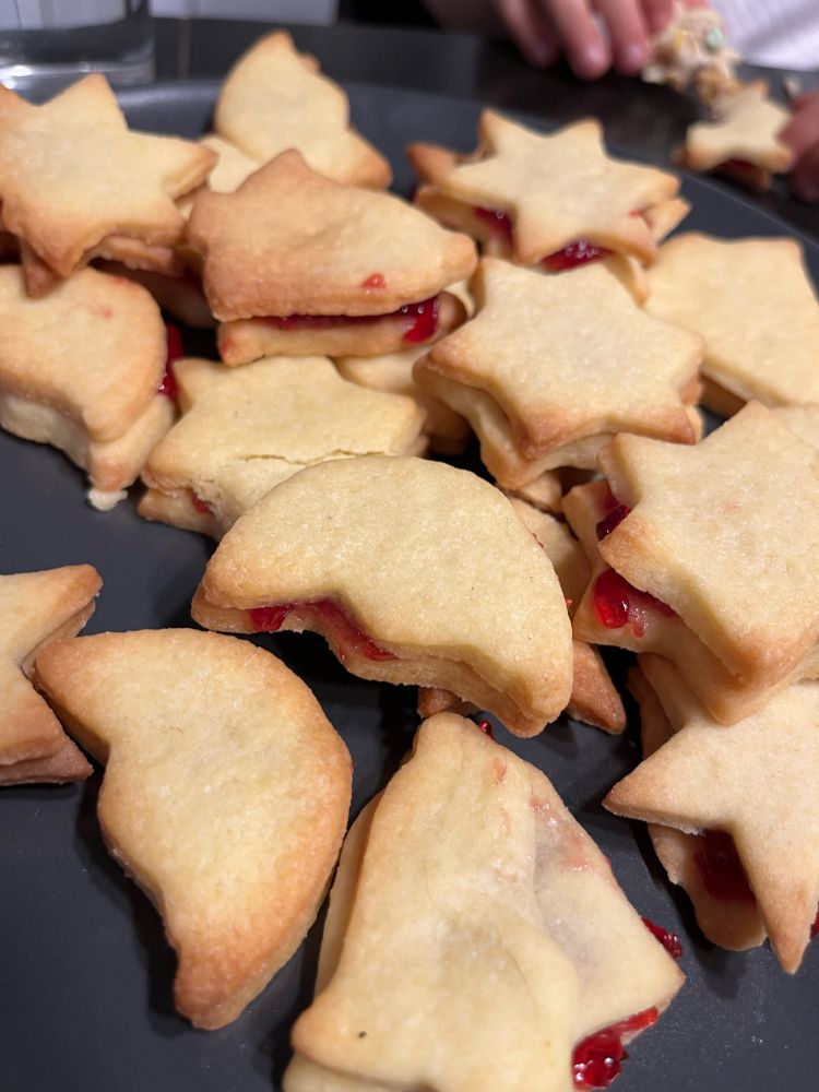 Ausgestochene Mürbeteigkekse in weihnachtlichen Formen, gestapelt mit roter Marmelade zwischen je zwei.