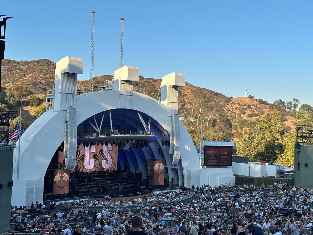 The stage at the Hollywood Bowl at sunset. The screen behind the stage has a graphic reading “J.C.S.”