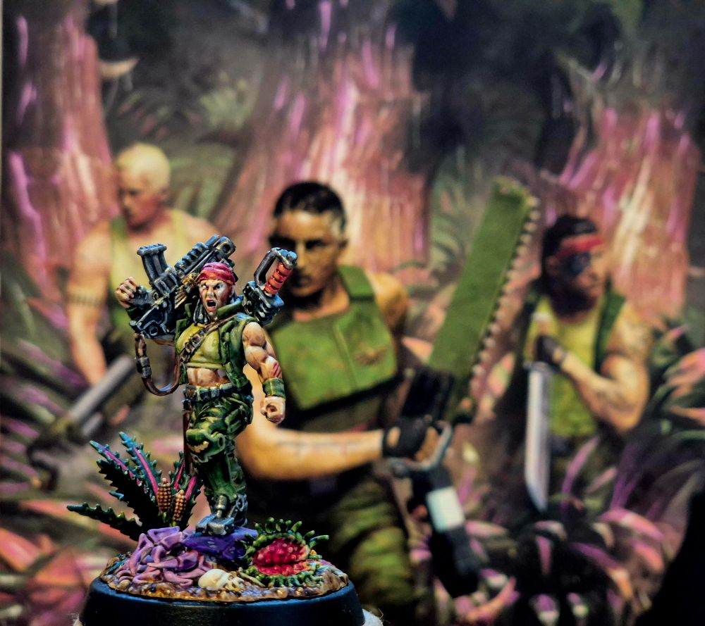 A painted Catachan Sergeant Ripper Jackson model in front of the cover of the Warhammer 40K novel Deathworlder 