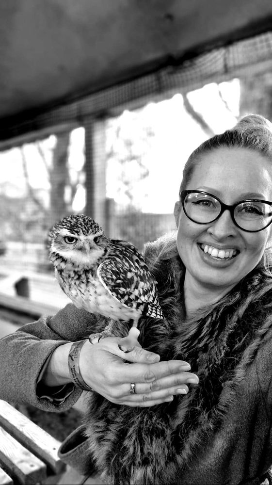 A black and white photo of Tory with a burrowing owl sitting on her hand