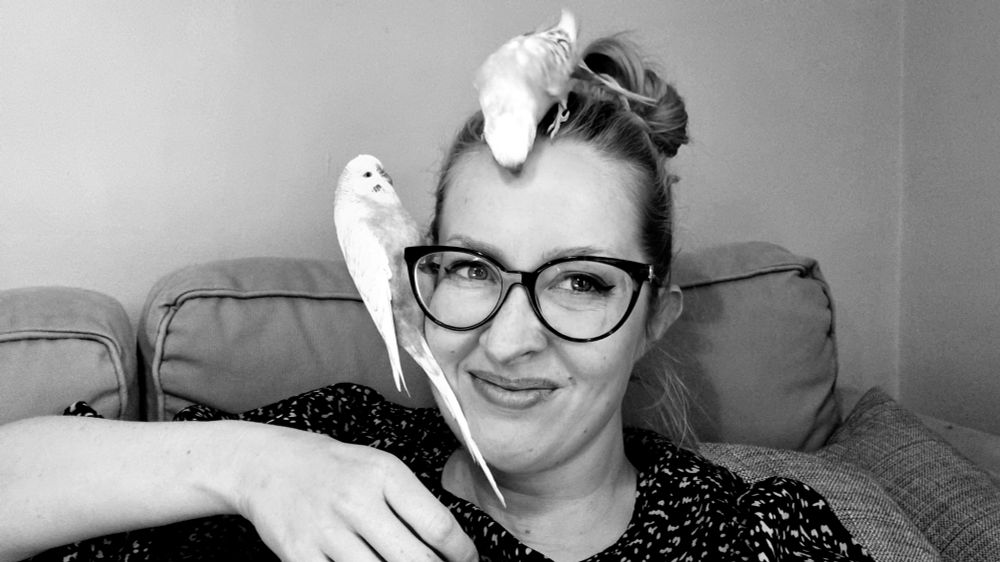A black and white photo of Tory's budgies perched awkwardly on her head and glasses