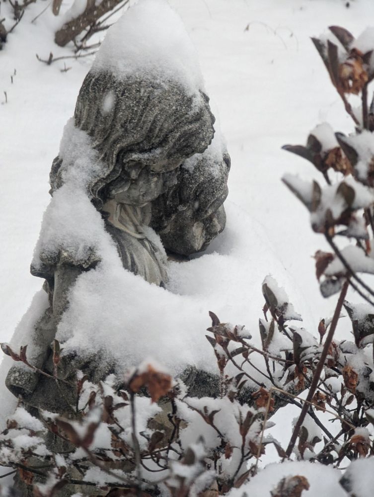 A garden sculpture of two young children embracing, covered in snow.