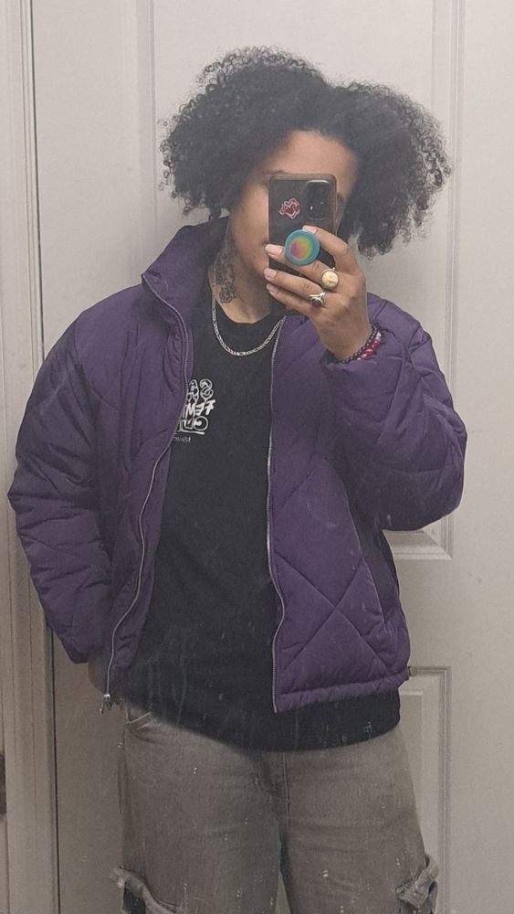 lilac looking casually handsome in a silver necklace layered over black "Sad Femme Club" tshirt under purple puffer jacket with gray cargo jeans.