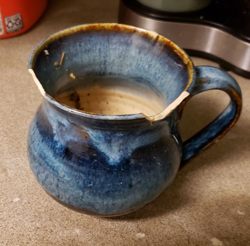 A blue gradient mug with two large chips broken off of the rim.