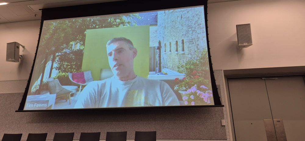 Tim Fawns against Italian-looking Zoom background, projected on a conference wall.