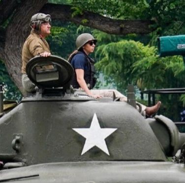 Two people casually sitting atop a tank’s turret kind of looking like people who stole a tank and accidentally stumbled into a parade