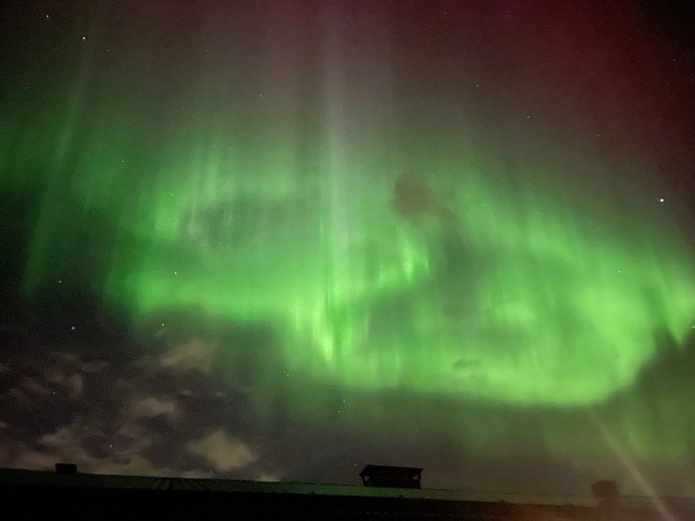 Bright green, with a hint of red, Northern lights above a rooftop. 