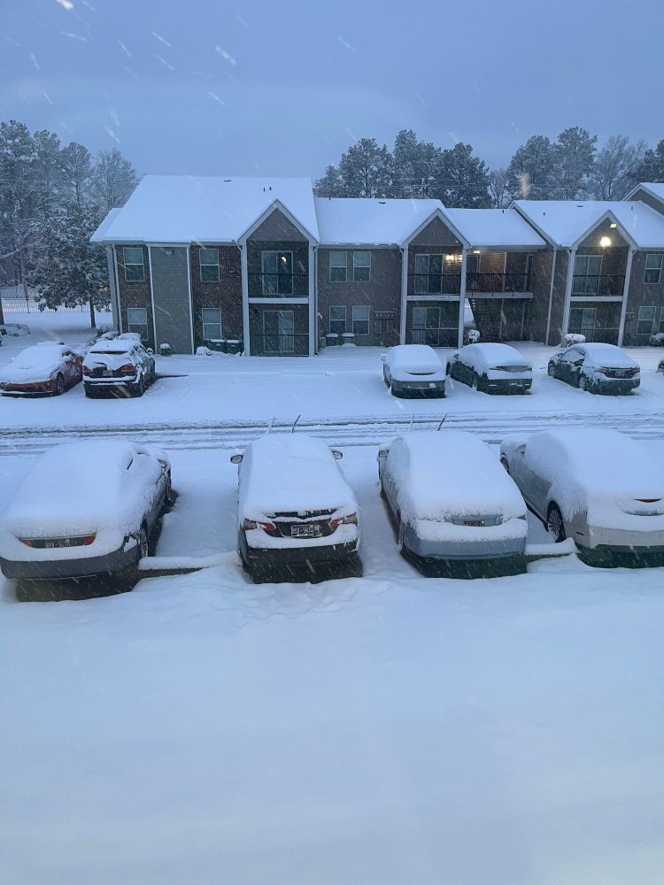 A parking lot at an apartment complex with a thick blanket of fresh snow on the ground. 