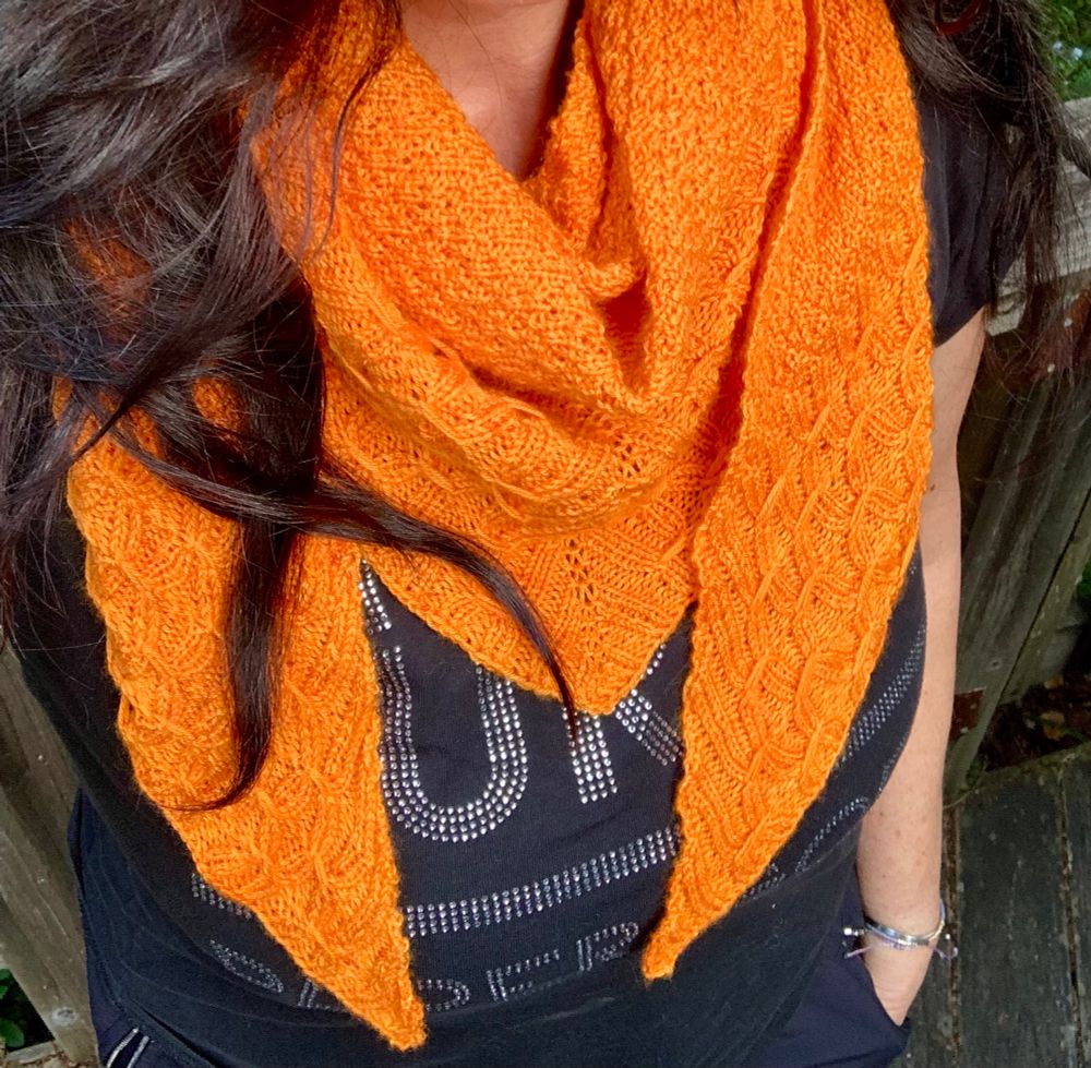 Woman wearing black shirt and orange hand knit shawl. Yarn from Lolabean  Yarn Company