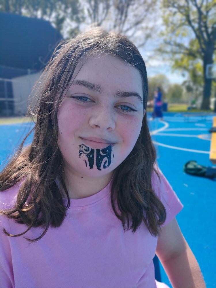 A young girl smiles showing off the temporary kirituhi (tattoo) on her chin. 