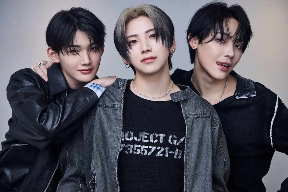 Jo, Yuma and Nicholas posing for Real Sound magazine. They're all wearing black dark outfits. Jo is leaning on Yuma's shoulder, with Nicholas standing next to Yuma (with his tongue out)