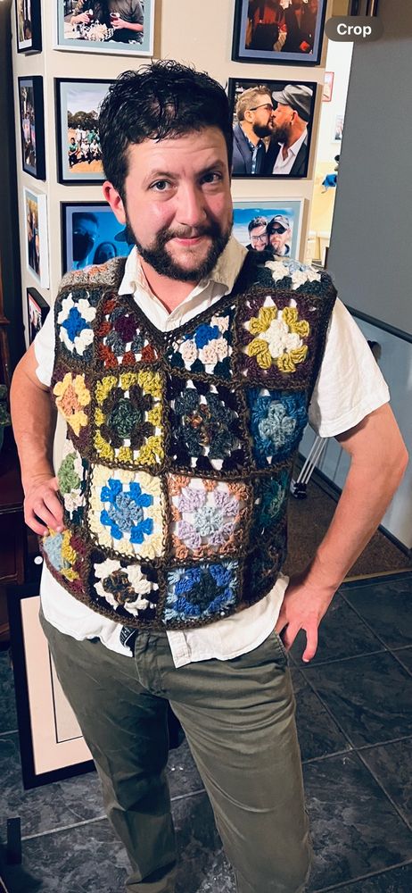 Emrys standing in linen shirt and olive pants modeling a wool sweater vest 