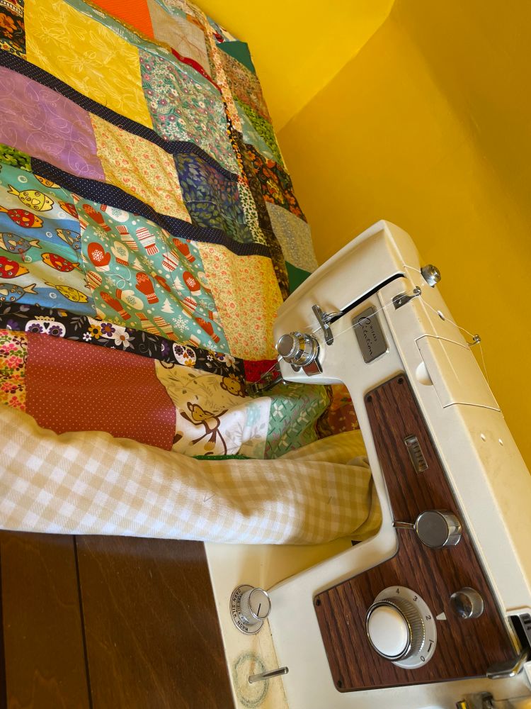 Top view of a vintage cream and wood grain designed sewing machine quilting a scrap quilt.