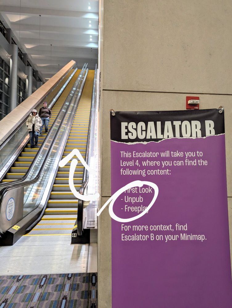 Escalator B on the second floor of the Philadelphia Convention Center, going up to the terrace. A banner indicates it's where attendees can find First Look, Unpub, and Freeplay