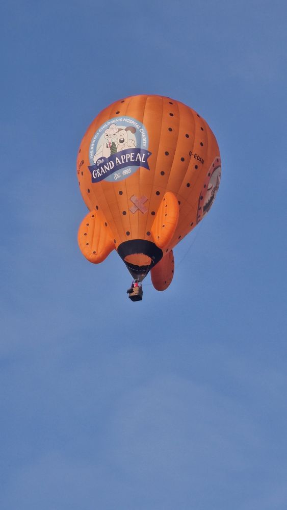 An orange hot air balloon in the shape of a rocket, with a picture of Wallace and Gromit staring out of a window on the side
