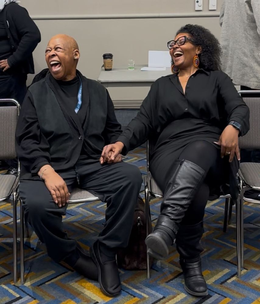 Two women seated, both laughing and smiling. 