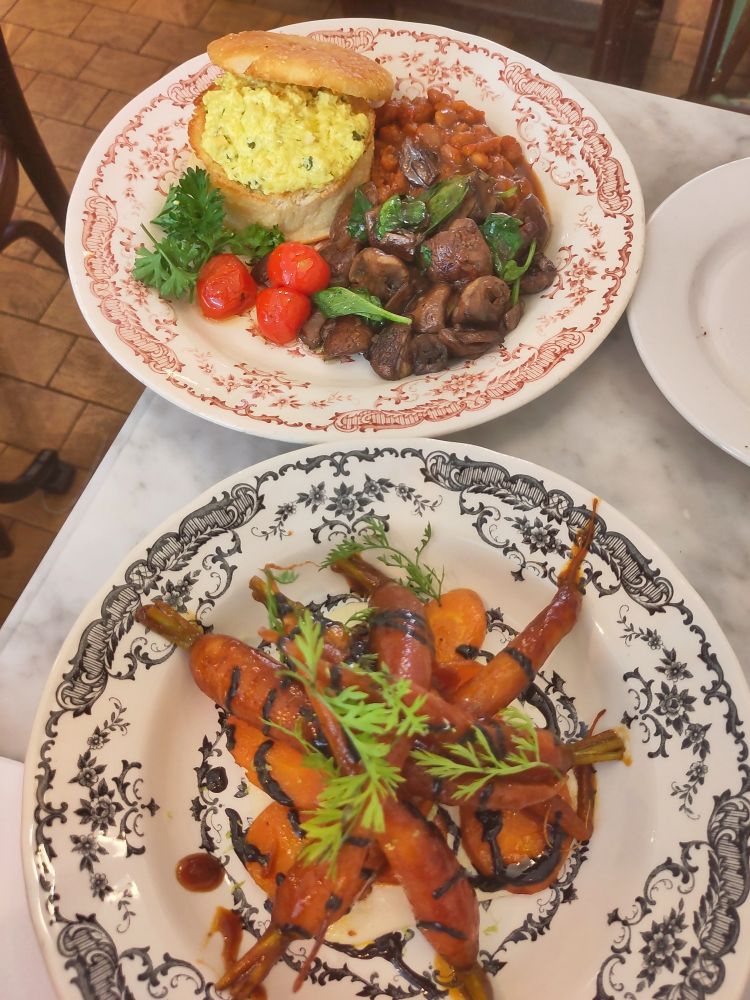 Assiette de carottes sauce barbecue avec une autre assiette contenant des champignons, des haricots, des tomates et un english muffin fourré de tofu brouillé 
