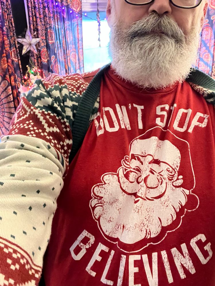 Bearded man wearing a sweater and red T-shirt with image of Santa Clause and text reading Don’t Stop Believing