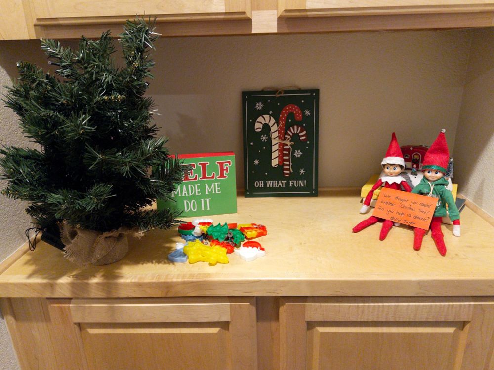 A counter top with a small tree, decorations, and two Elves with a note