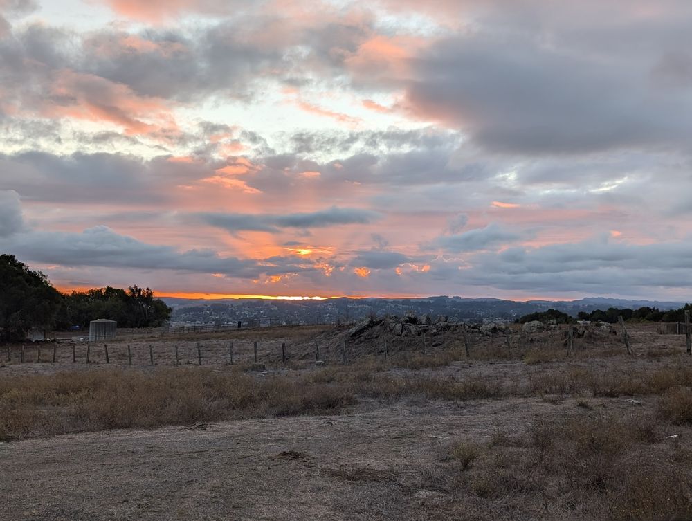 Sunset turning clouds orangey red, looking out over some rocky farmland.
