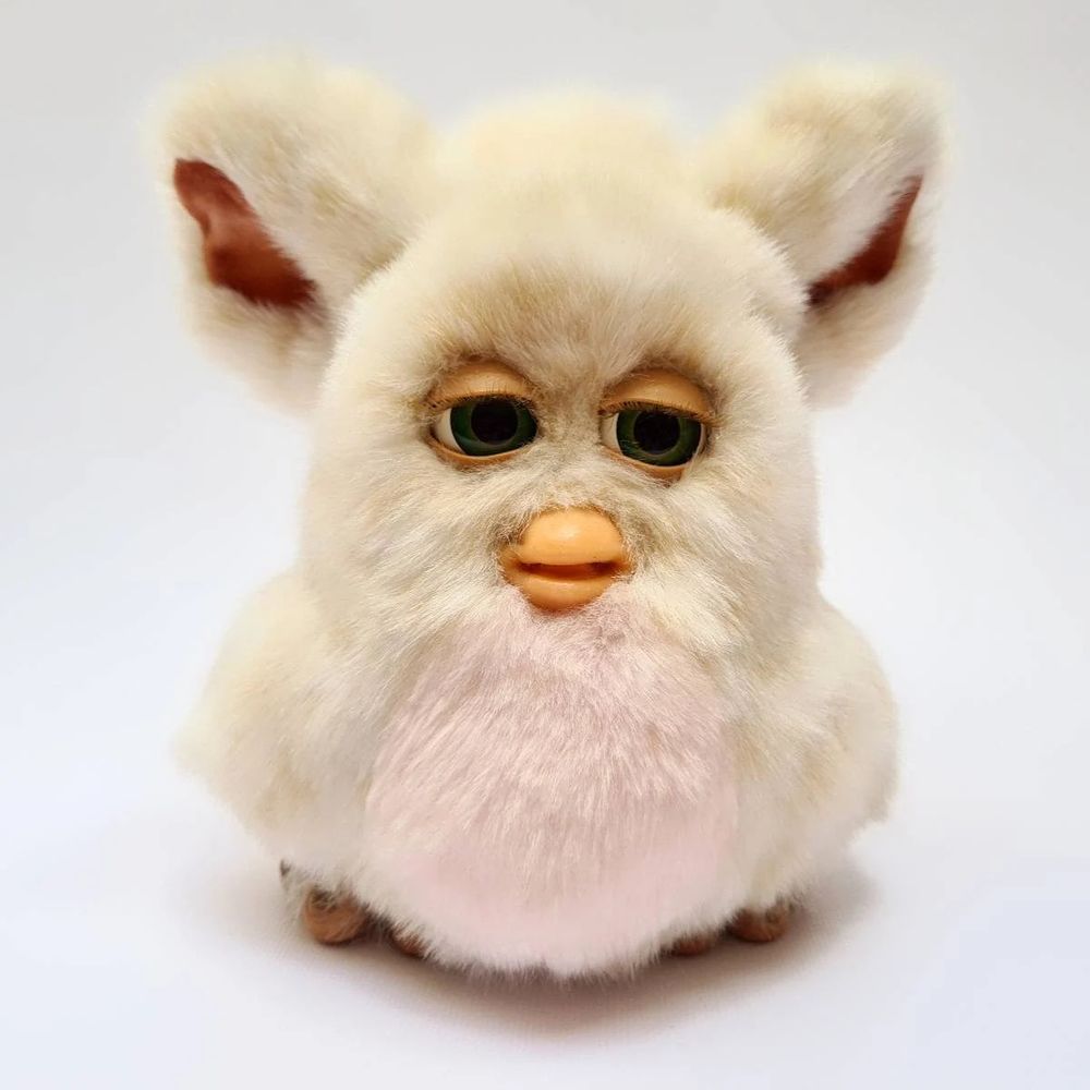 A photo of the 2005 Furby.  Its fur is cream with a pink belly.  Its eyes and beak are fleshy.