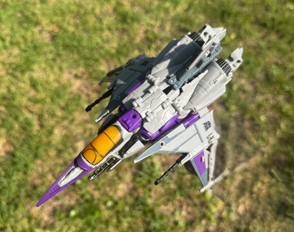 Skywarp, in jet mode, flying above some grass.