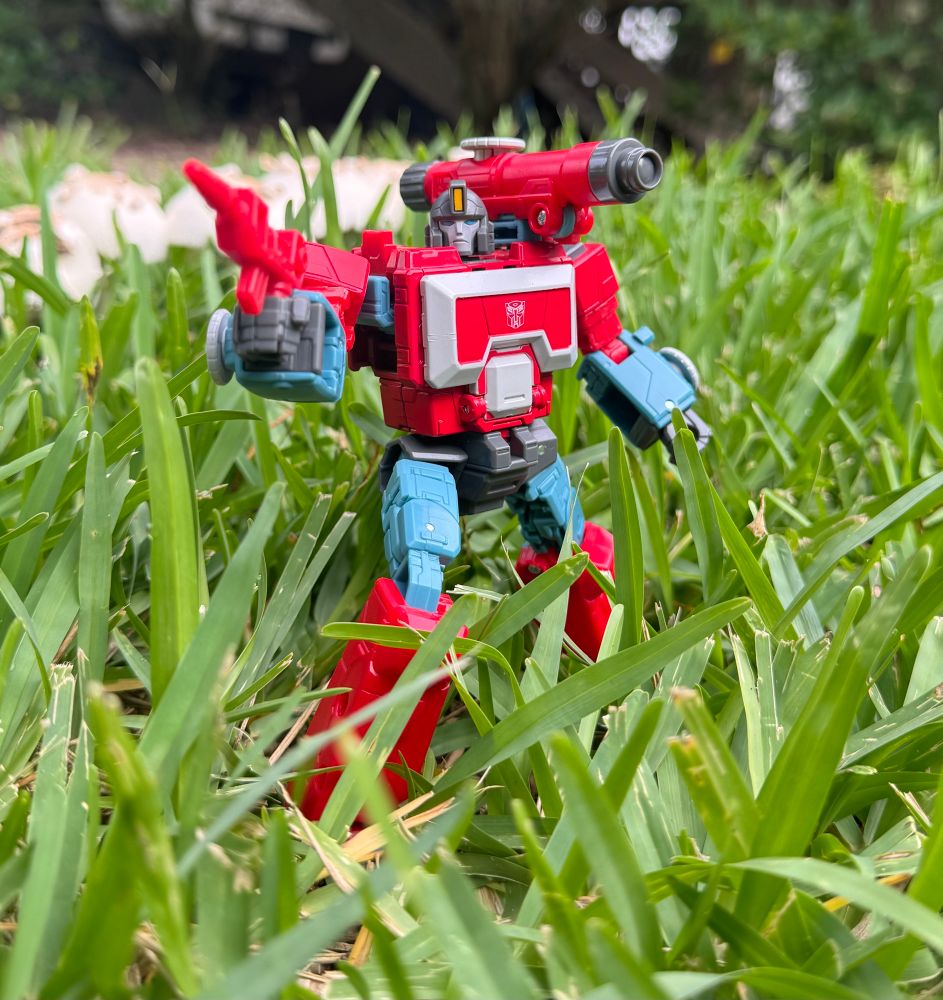 Perceptor standing in tall grass with is blaster in hand.