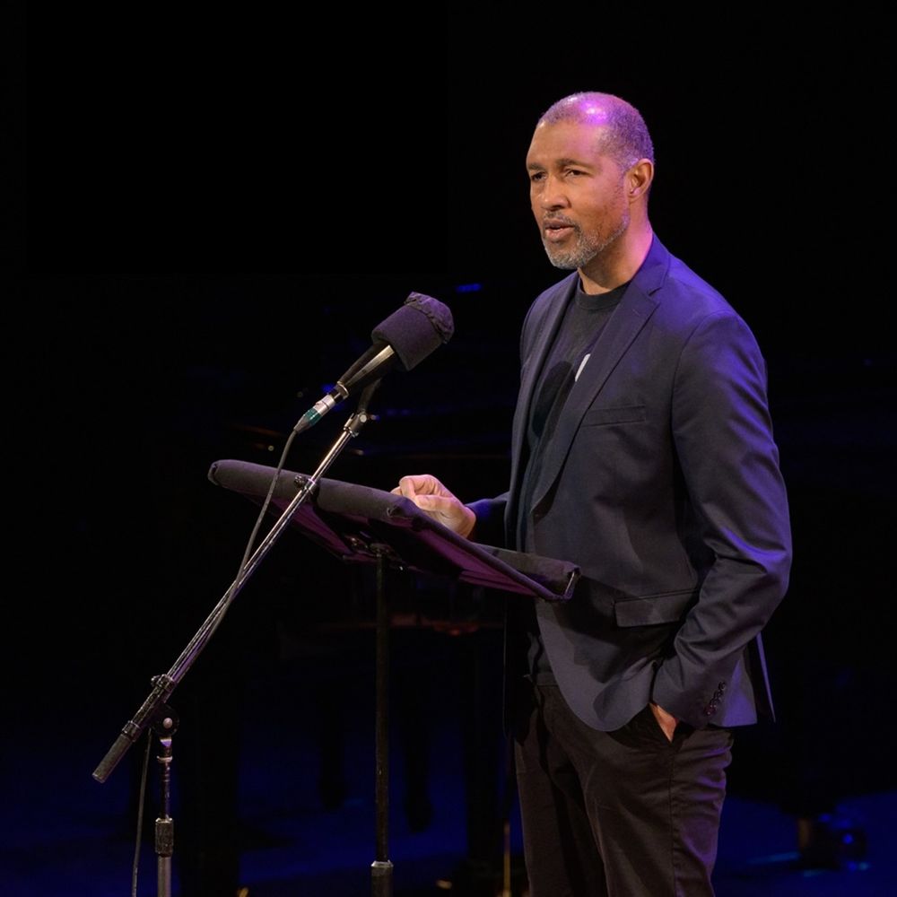 Dion Graham stands on the stage in front of a microphone reading a story.