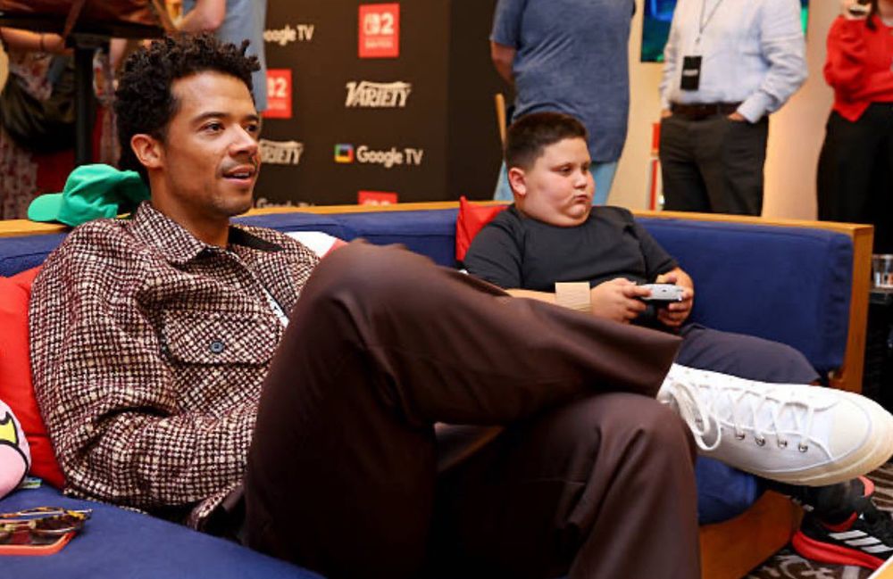 Jacob Anderson and The Rizzler sharing a couch playing video games during comic con