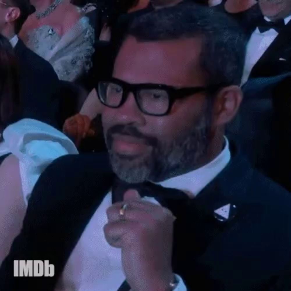 a man wearing glasses and a tuxedo is sitting in a crowd with imdb written above him