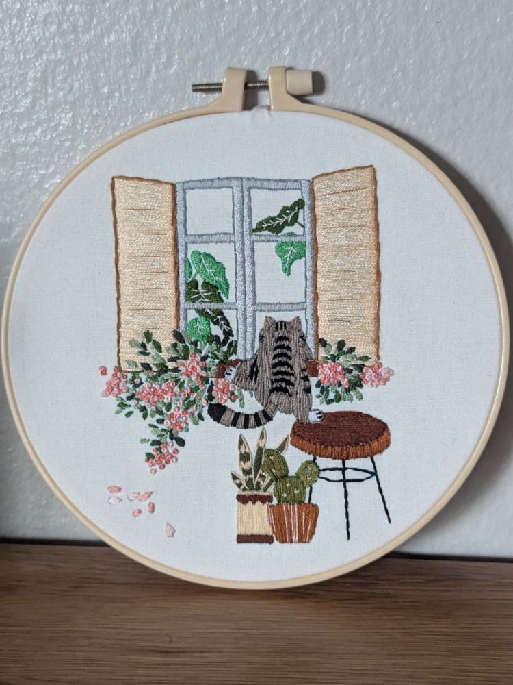 Embroidery pattern of tabby cat climbing window with florals and plants 
