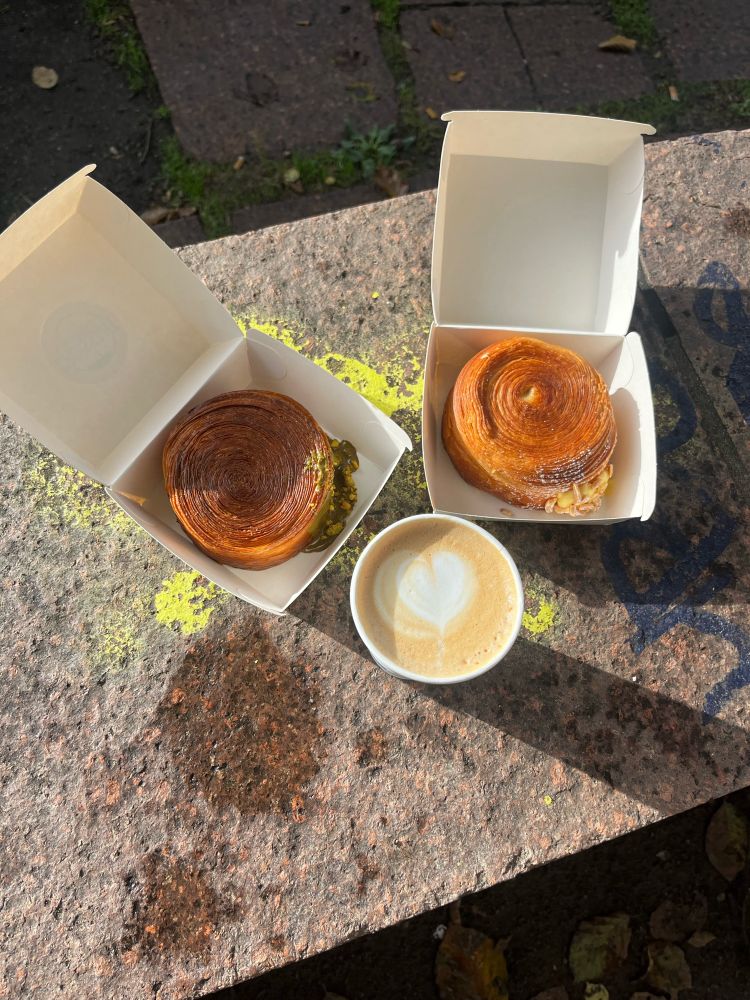 ein bild von zwei croissants taschen und einem cappuccino auf einer stein bank im park