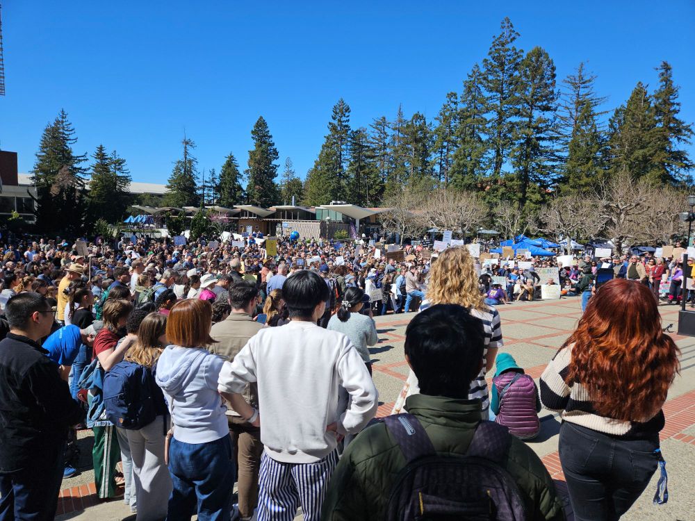 Large crowd holding signs on the UC Berkeley campus with open space in the middle.