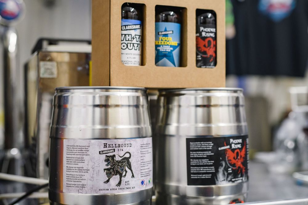 Two small metal kegs with a gift pack of beer bottles balanced on top. In the background is beer dispense and merchandise.