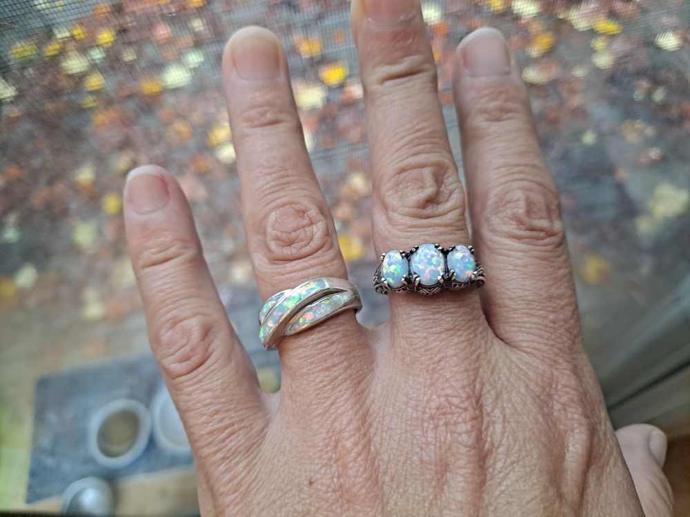 My hand witn two opal rings. The leftmost one has opal bands in swirl.  The one on the right has three stones.  