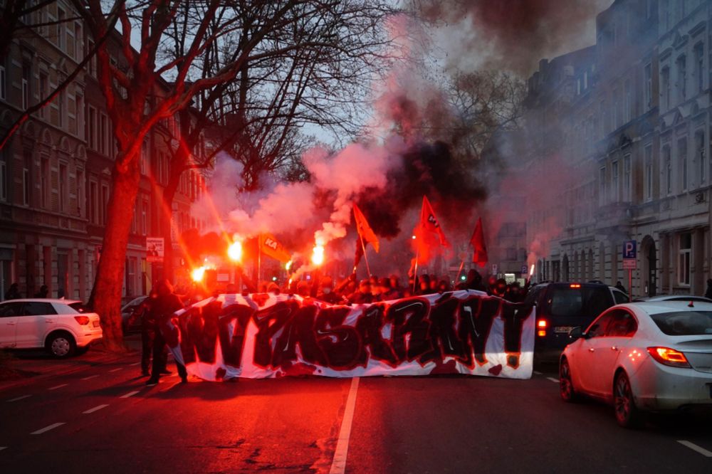 NO PASARAN! Frontbanner der Blockade. Dahinter: Menschenmenge mit roten Bengalos und schwaren Rauchtöpfen