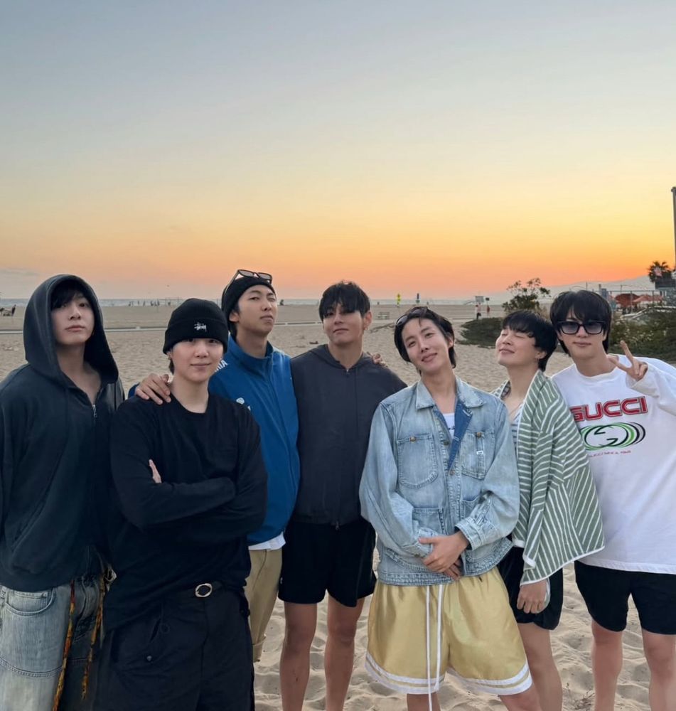 BTS reunido em uma foto na praia, com o sol se pondo no fundo. Eles aparecem na sequência, da esquerda para a direita: Jungkook, Yoongi, Namjoon, Taehyung, Hoseok, Jimin e Seokjin. 