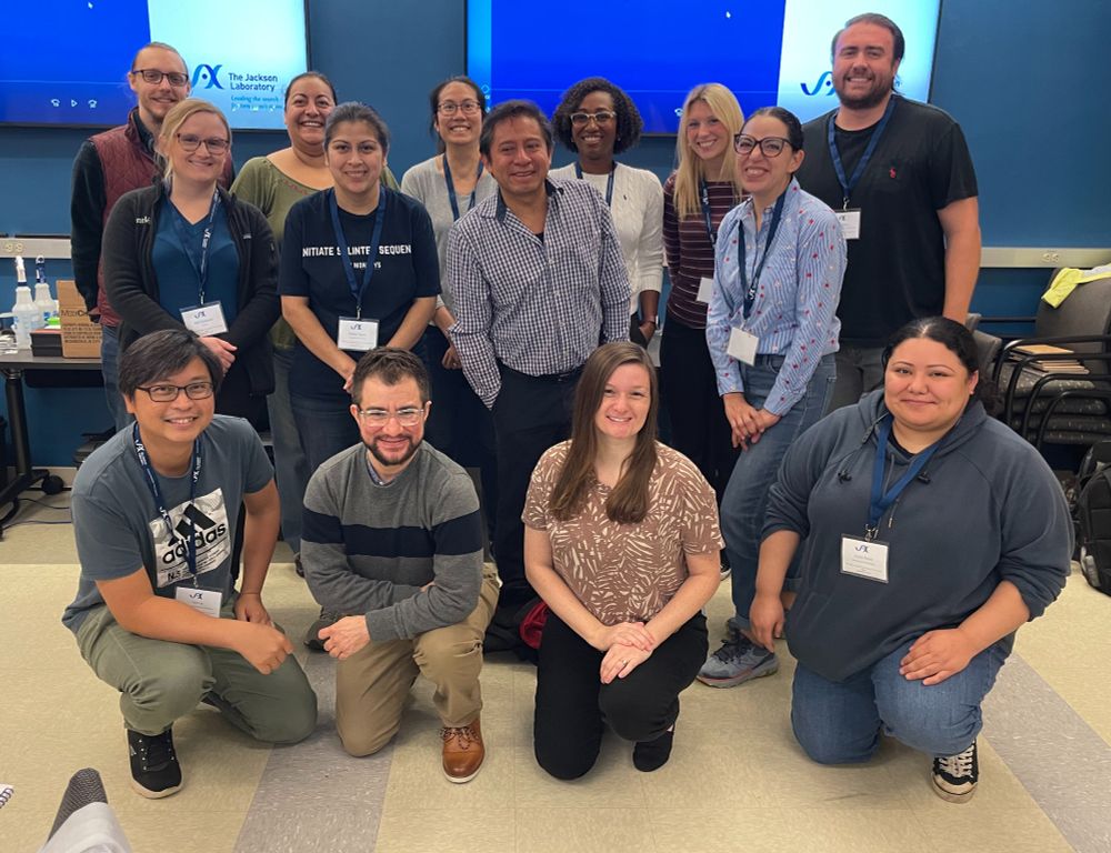 Surgical workshop participants pose for a group photo in front of two large blue television screens.