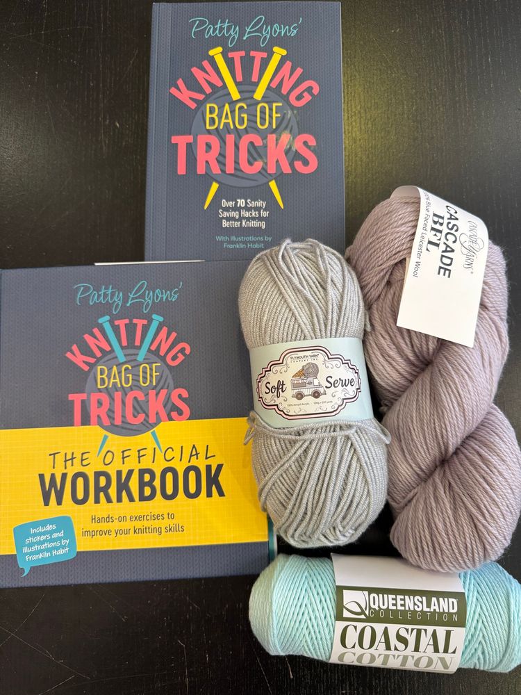 Against a black table my supplies:  Patty Lyons’ Bag of Tricks book and workbook, plus a skein of wool (Cascade BFL) in gray, a skein of acrylic (Plymouth Soft Serve in gray), & a skein of cotton (Queensland Coastal Cotton in mint green pastel).