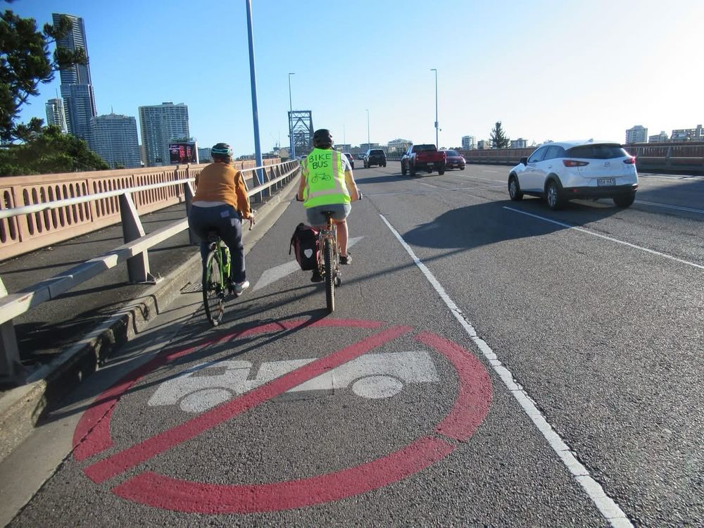 Cyclists ride in the side lane over a no-trucks sign on the road.  