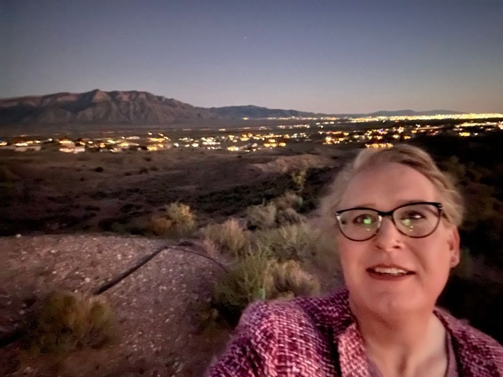 Me in foreground with the city of Albuquerque in the evening, lights shining, at the base of the Sandia mountains.