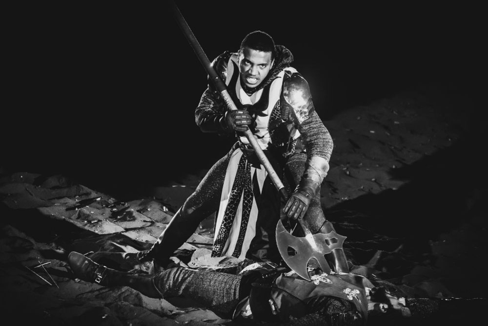 A medieval knight (actor) holding a halberd to another.