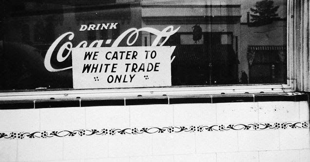 A sign on a diner window, over a Coca-Cola advertisement, that reads "WE CATER TO WHITE TRADE ONLY"
