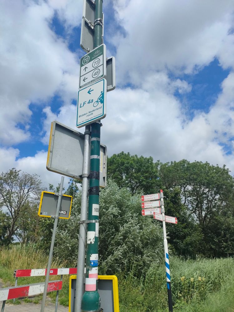 Photo d'une intersection de deux pistes cyclables entre Woerden et Utrecht. Les points-nœuds verts figurent sur le poteau au premier plan, les panneaux directionnels rouges sur le poteau au deuxième plan.