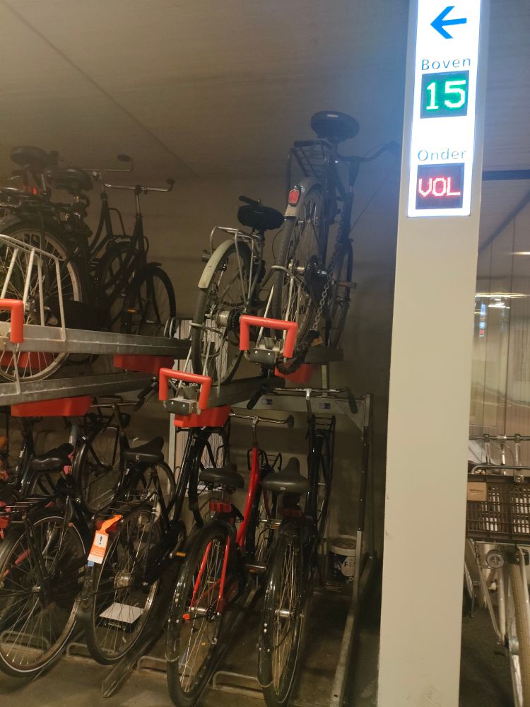 Quelques vélos garés au parking vélo de la gare centrale d'Utrecht. Un compteur indique 15 places disponibles sur les racks du haut et "VOL" (complet) sur les racks du bas.