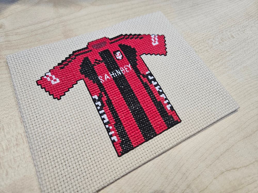 Cross stitch version of Gaziantep FK shirt (red body with three thick vertical black stripes on the body, the outer stripes are curved on one side to link with the sponsor logos on the sides, red sleeves and collar)