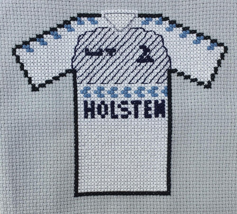 Cross stitch version of retro Spurs shirt, white with dark blue diagonal thin pinstripes on top half of body, below that lighter blue arrows and large dark blue 'holsten' sponsor logo
