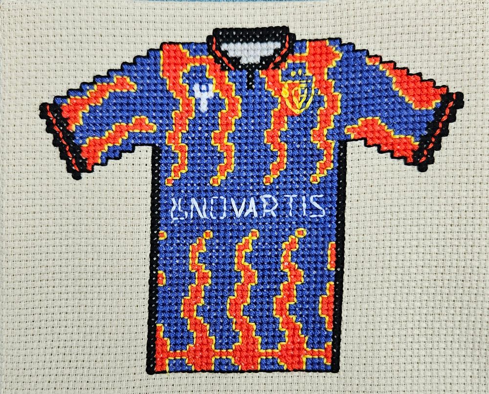 Cross stitch version of last season's fc basel shirt, blue body with flame effect stripes (think those slipknot shirts that kids in the 2000s wore) that are red, with yellow trim. Black collar and cuffs with red trim. 