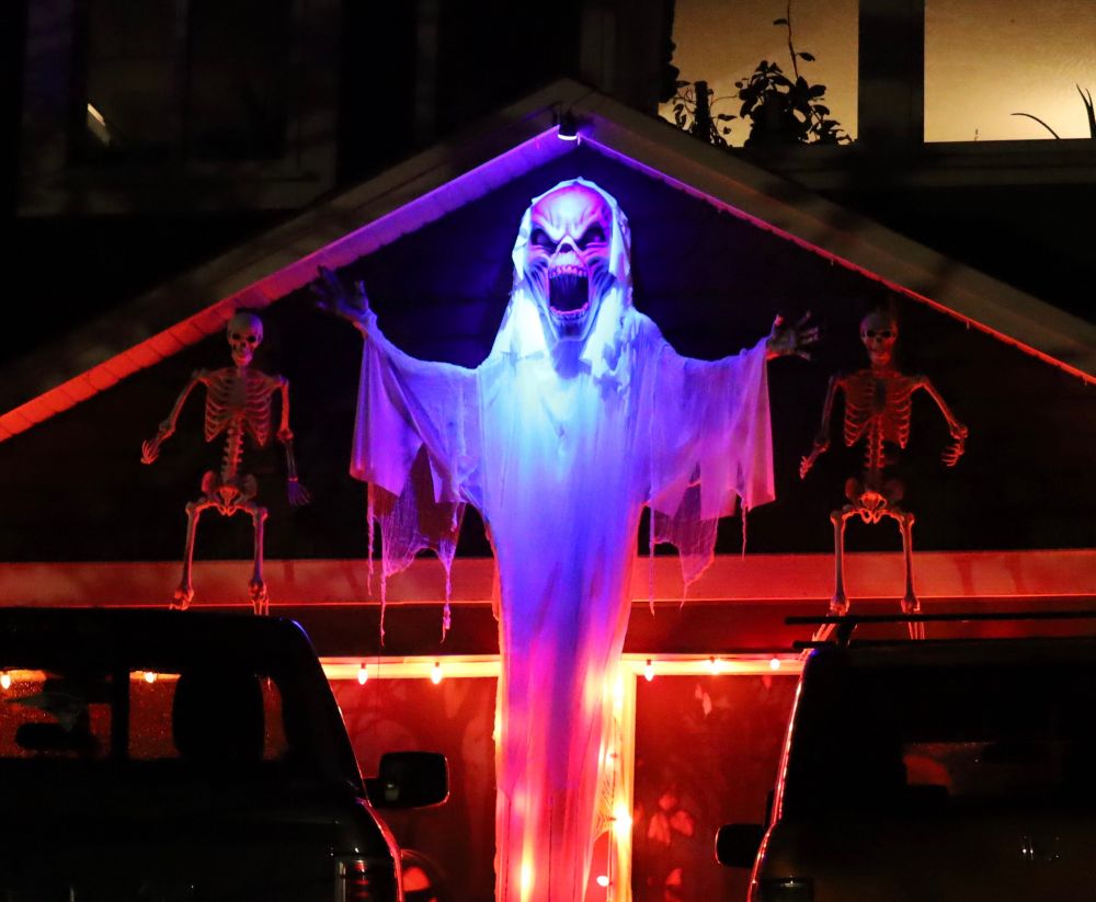 A screaming demon on the front of a house flanked by skeletons and creepy lighting. 